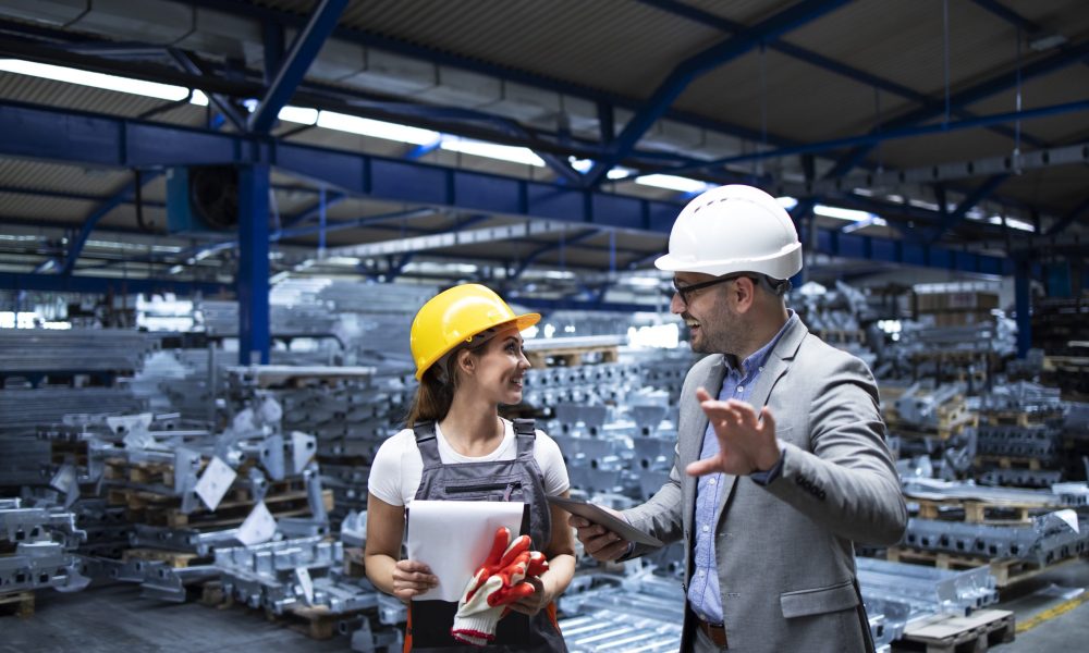 Manager wearing hardhat and industrial worker discussing about production in metal factory.
